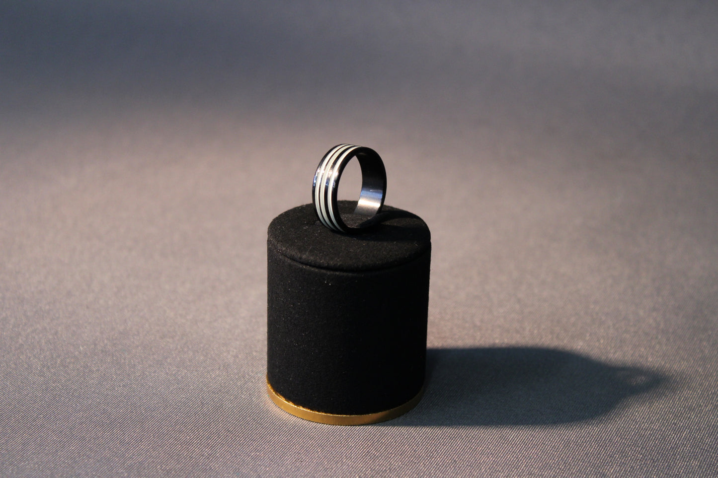 Mustanvärinen sormus, jossa kolme uraa, koko 19 mm, esillä mustalla korualustalla.