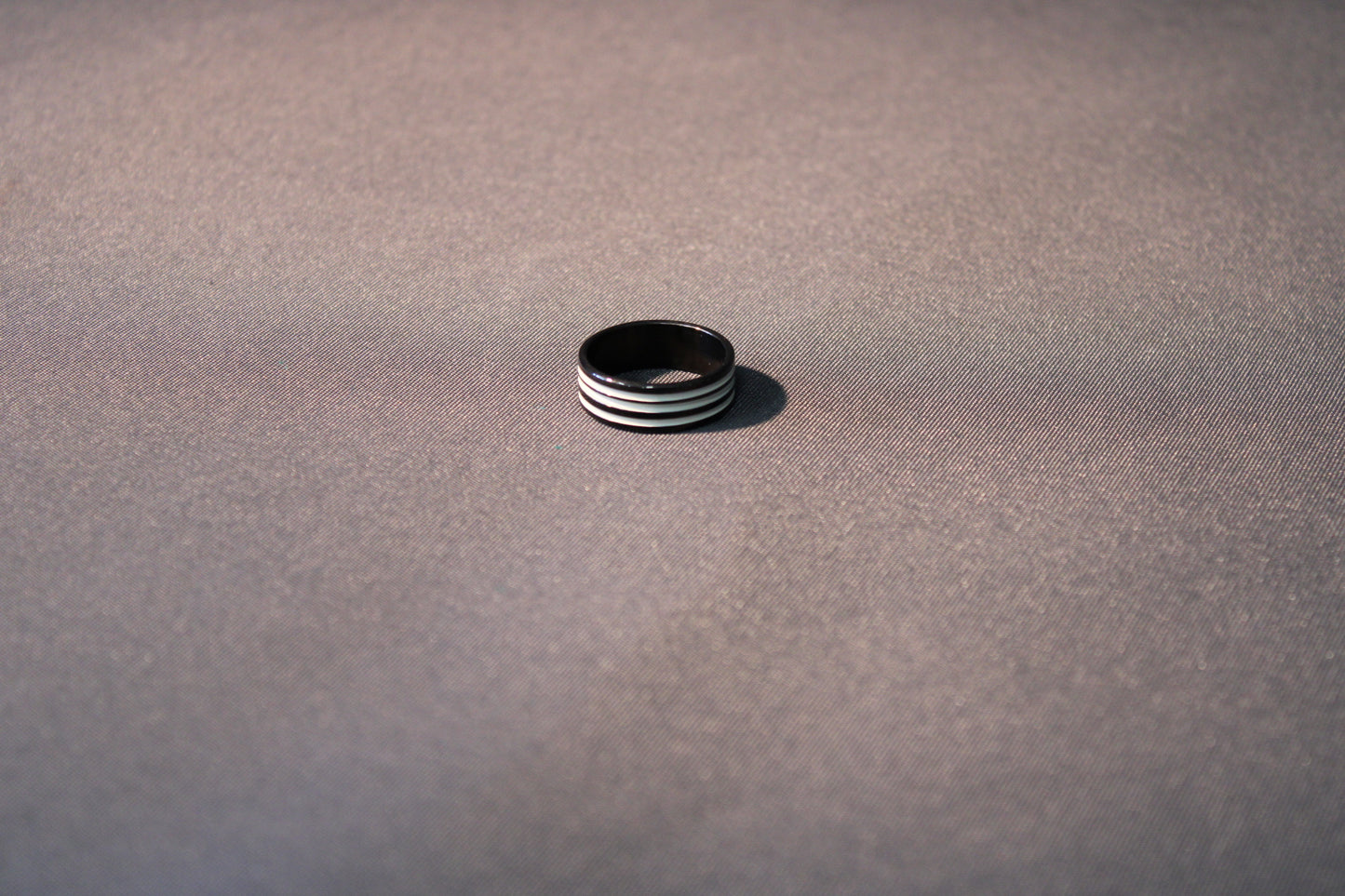 Sormus, mustan värinen kolmella uralla, koko 19 mm, kuvattuna harmaalla taustalla.