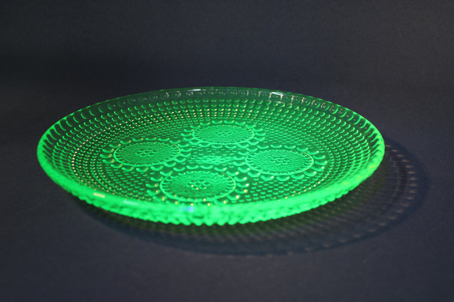 Grapponia-lautanen UV-valossa, vihreä uranilasi hehkuu kirkkaasti.