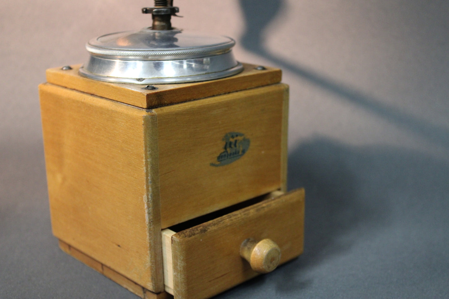 Kahvimyllyn etuosa, puinen laatikko ja vintage-logo lähikuvassa