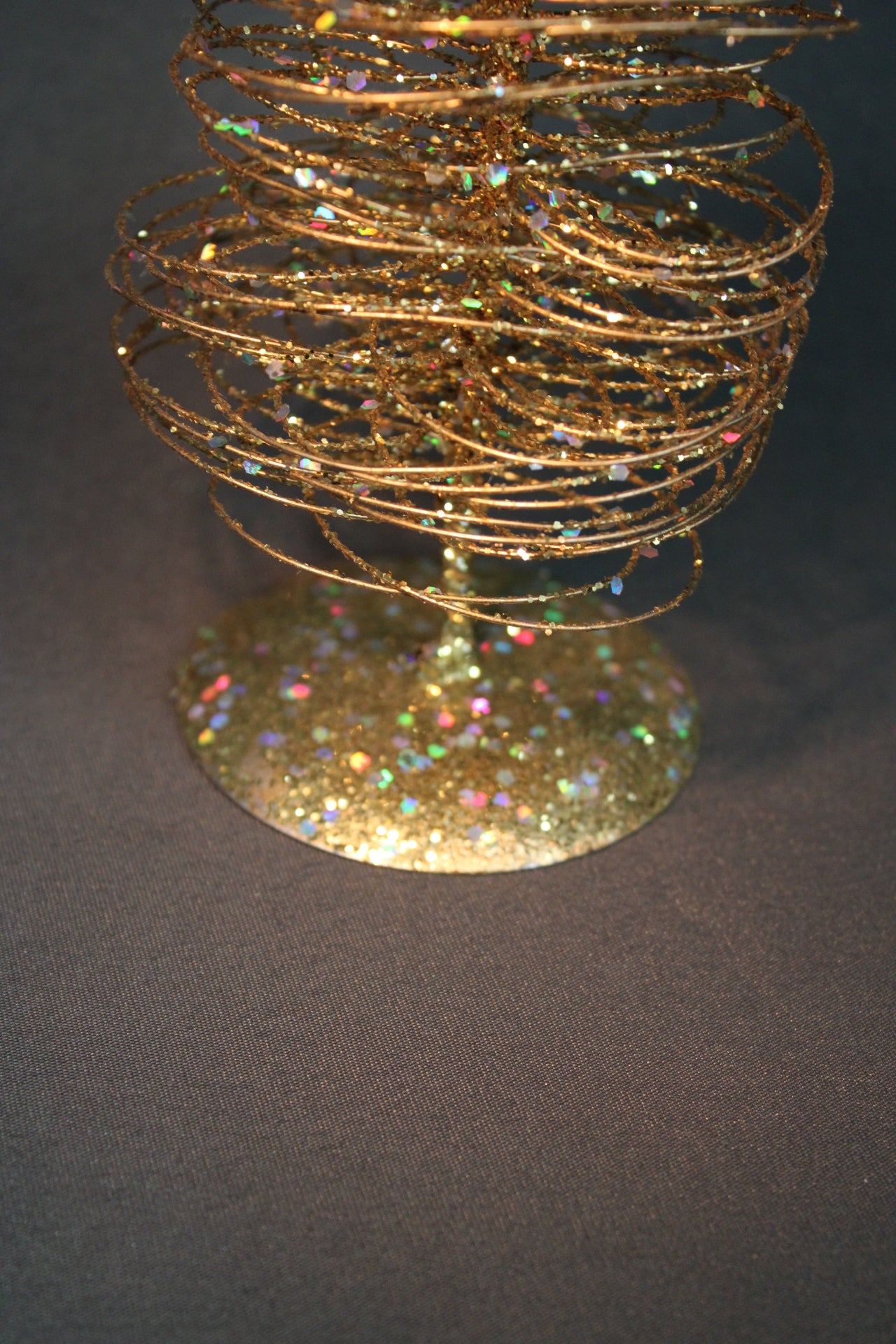 Kultaisen koristekuusen jalusta ja glitterpinta lähikuvassa