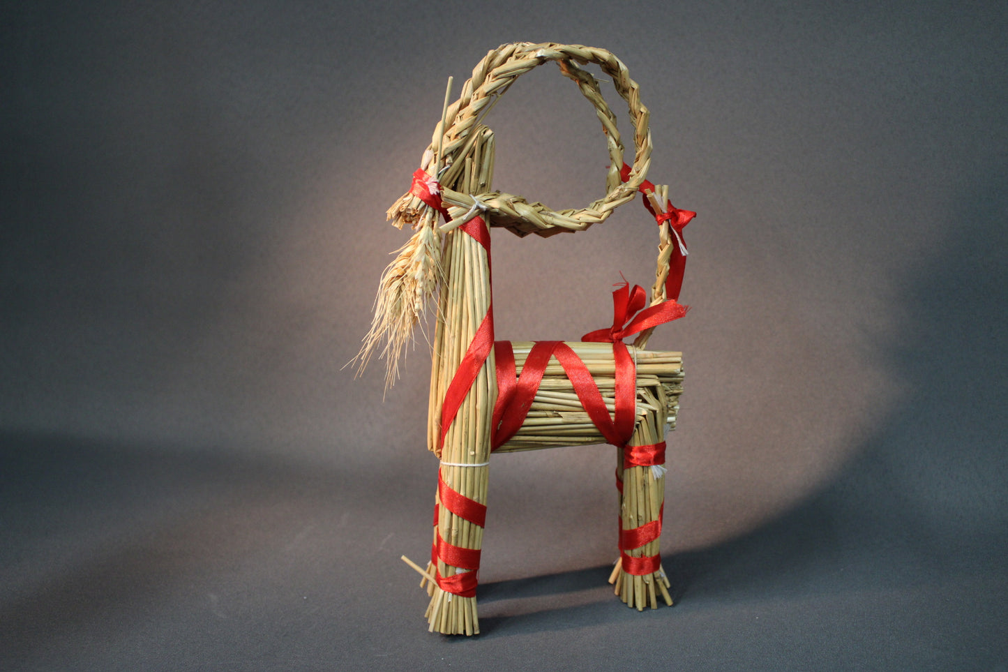 Olkipukki sivulta, oljista punotuilla yksityiskohdilla ja punaisin nauhoin