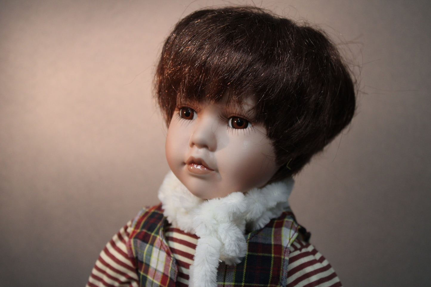 Lähikuva posliininukke pojasta, ruskeat hiukset ja ruutuliivi.