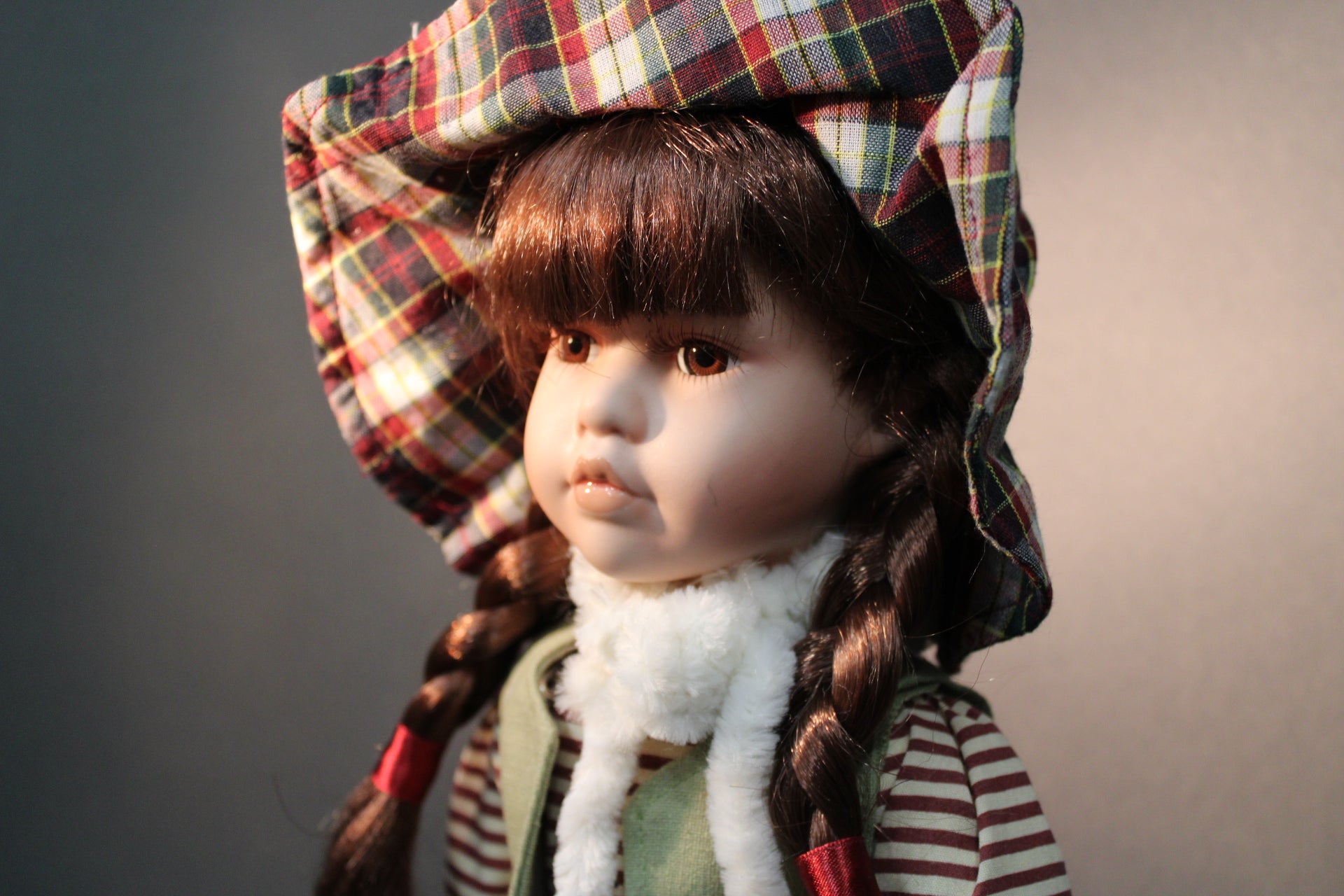 Posliininuken kasvojen lähikuva, tytönukke 40 cm, ruskeat letit ja ruutupäähine.