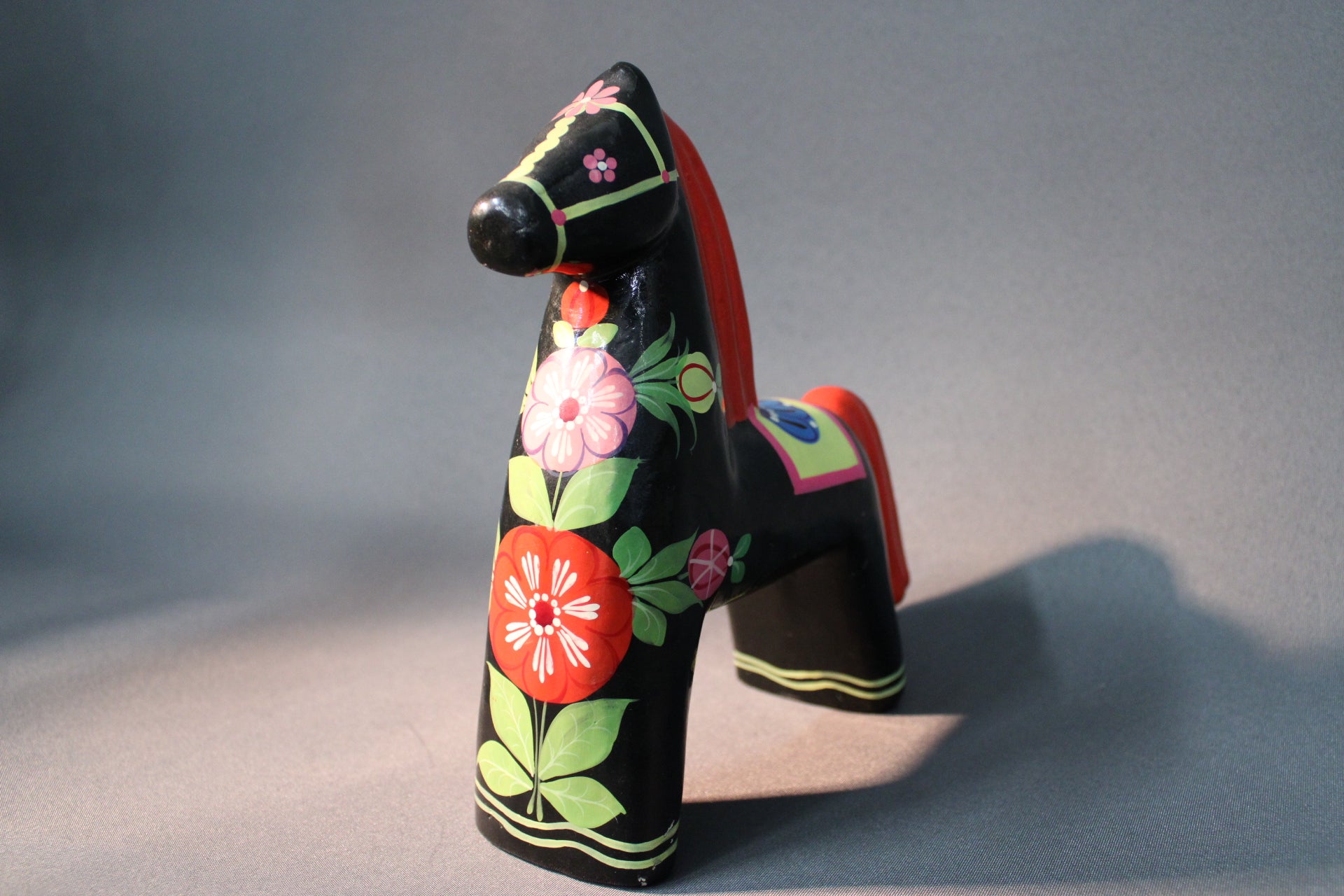 Käsin maalattu puuhevonen, musta pohja ja värikäs kukkakoristelu, perinteinen puuesine