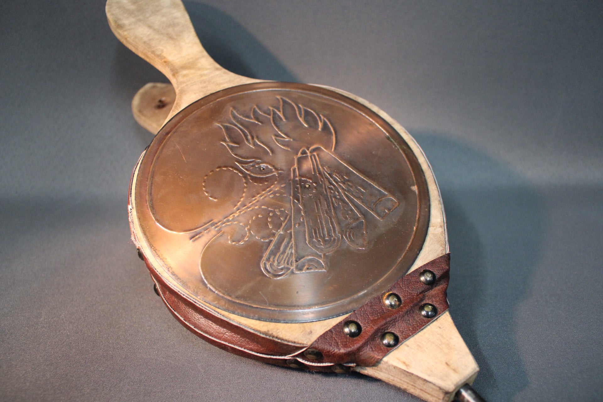 Takkapalkeen metallinen koristelevy, liekki- ja halkokuvio, puu ja nahka