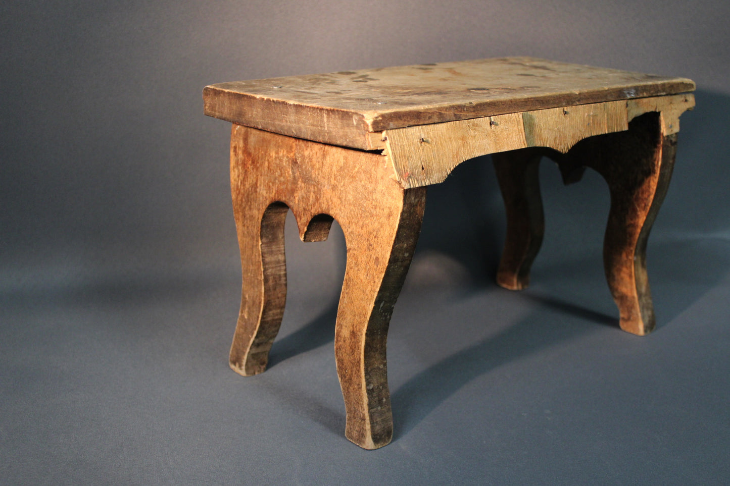 Vanha puinen jakkara viistosta kuvattuna, epätasainen patina ja käytön jäljet