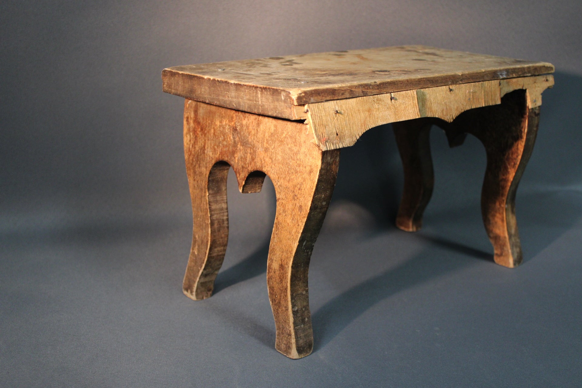 Vanha puinen jakkara viistosta kuvattuna, epätasainen patina ja käytön jäljet